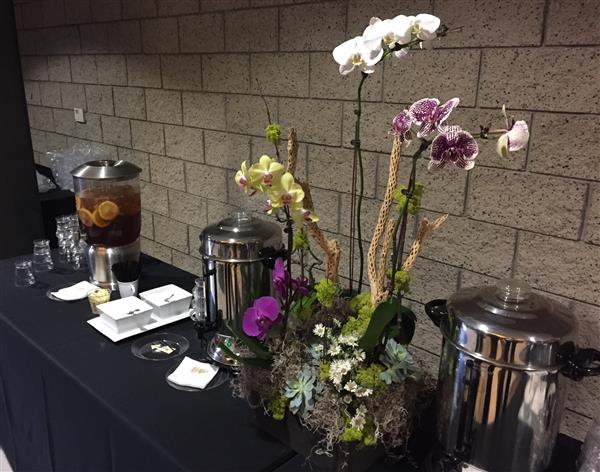 Orchid and succulent flower arrangement on table with tea and coffee dispensers